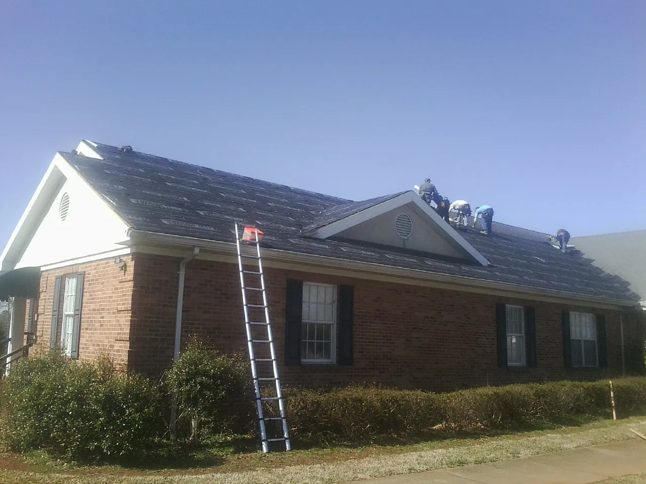 Crew tearing shingles off a brick ranch roof with a ladder set — Metal Roof Repair work by our crew in Lincoln City