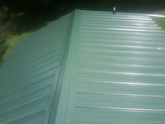 New green metal panels meeting at the ridge of a roof — Flat Roof Repair work by our crew in Lincoln City